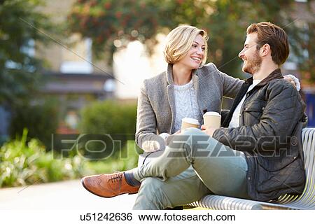 Stock Photograph - Couple Relaxing On Park Bench With Takeaway Coffee. Fotosearch