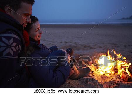 Stock Photography - Couple Sitting By Fire On Winter Beach . Fotosearch
