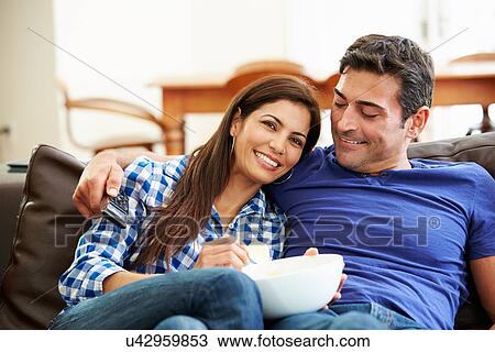 Stock Image - Couple Sitting On Sofa Watching TV Together. Fotosearch