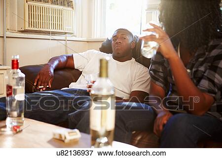 Stock Photo - Couple Sitting On Sofa With Bottle Of Vodka And Cigarettes. Fotosearch