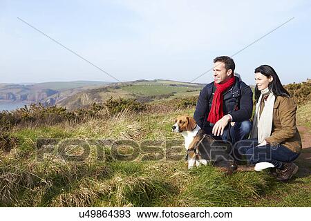 Stock Image - Couple With Dog Walking Along Coastal Path. Fotosearch