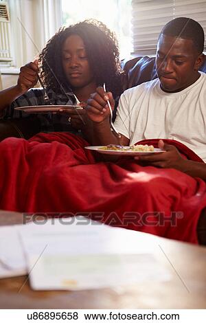 Stock Photo - Couple With Poor Diet Sitting On Sofa Eating Meal. Fotosearch