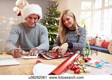 Stock Image - Couple Wrapping Christmas Gifts At Home. Fotosearch