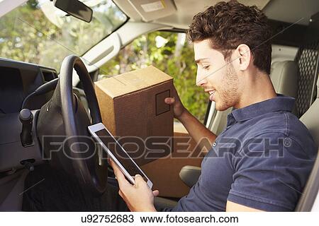 Stock Image - Delivery Driver Sitting In Van Using Digital Tablet. Fotosearch