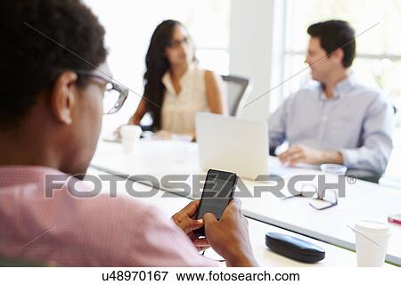 Designer Using Mobile Phone During Meeting View Large Photo Image Stock Photo - Designer Using Mobile Phone During Meeting. Fotosearch