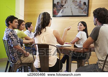 Stock Photograph - Designers Sitting Around Table In Meeting Looking At Screen. Fotosearch
