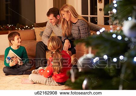 Stock Photo - Family Exchanging Gifts By Christmas Tree. Fotosearch