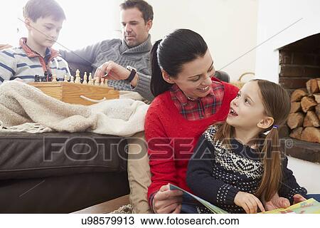 Stock Image - Family Relaxing Indoors Playing Chess And Reading Book. Fotosearch