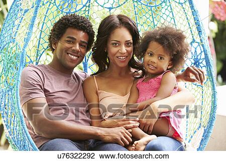 Stock Image - Family Relaxing On Outdoor Garden Swing Seat. Fotosearch