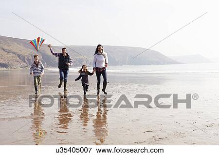 Stock Photo - Family Running Along Winter Beach Flying Kite. Fotosearch