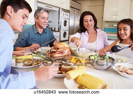 Stock Image - Family Sitting Around Table At Home Eating Meal. Fotosearch