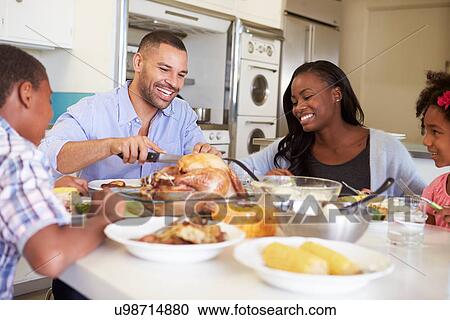 Stock Image - Family Sitting Around Table At Home Eating Meal. Fotosearch