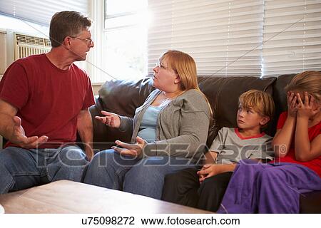 Stock Image - Family Sitting On Sofa With Parents Arguing. Fotosearch