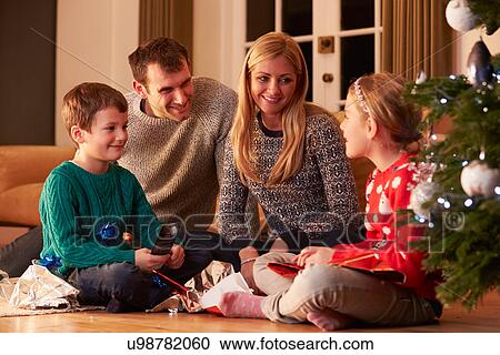 Stock Image - Family Unwrapping Gifts By Christmas Tree. Fotosearch