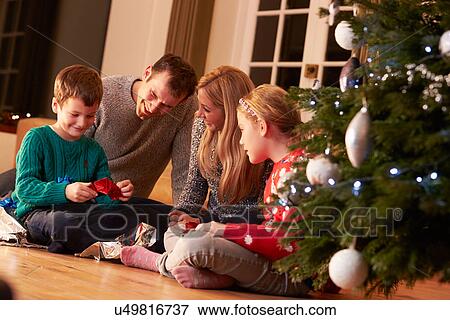 Stock Photo - Family Unwrapping Gifts By Christmas Tree. Fotosearch