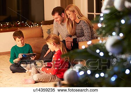Stock Photography - Family Unwrapping Gifts By Christmas Tree. Fotosearch