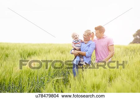 Picture - Family Walking In Field Carrying Young Baby Son. Fotosearch