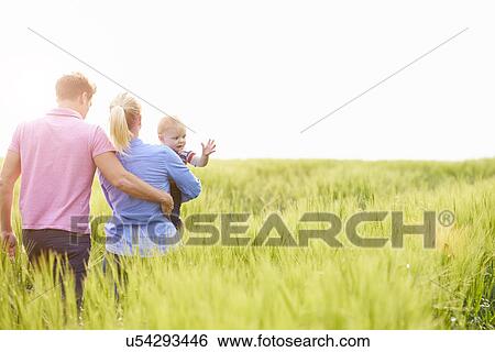 Stock Photograph - Family Walking In Field Carrying Young Baby Son. Fotosearch