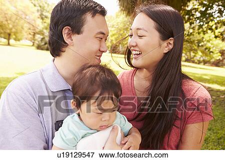 Stock Photo - Family With Baby In Carrier Walking Through Park. Fotosearch