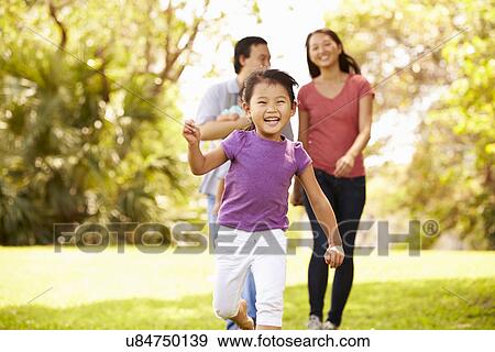 Stock Photo - Family With Baby In Carrier Walking Through Park. Fotosearch