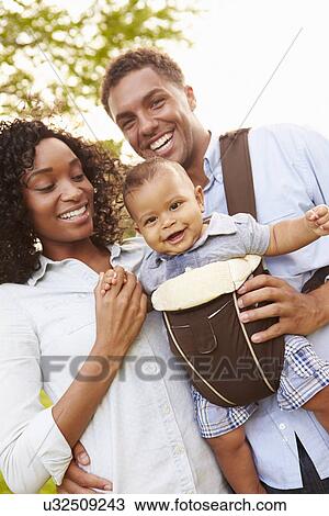 Stock Image - Family With Baby Son In Carrier Walking Through Park. Fotosearch