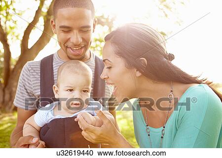 Stock Image - Family With Baby Son In Carrier Walking Through Park. Fotosearch
