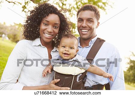 Stock Image - Family With Baby Son In Carrier Walking Through Park. Fotosearch