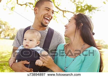 Stock Photo - Family With Baby Son In Carrier Walking Through Park. Fotosearch
