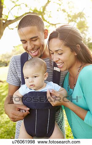 Stock Photo - Family With Baby Son In Carrier Walking Through Park. Fotosearch