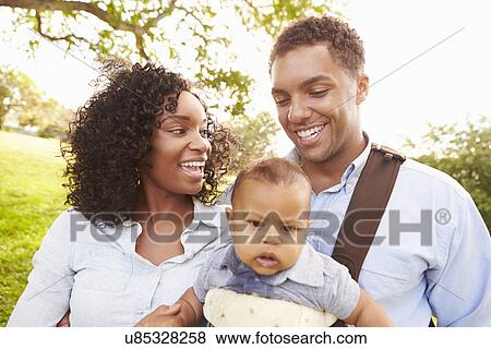 Stock Photo - Family With Baby Son In Carrier Walking Through Park. Fotosearch