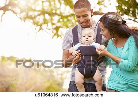 Stock Photograph - Family With Baby Son In Carrier Walking Through Park. Fotosearch