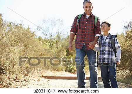 Stock Photo - Father And Son Hiking In Countryside Wearing Backpacks. Fotosearch
