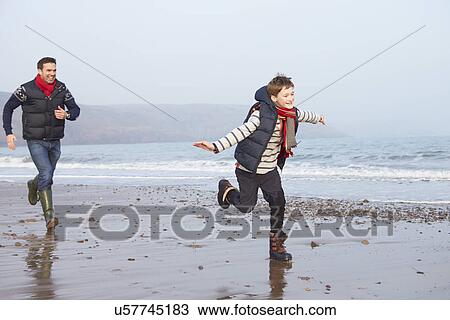Stock Image - Father And Son Running On Winter Beach. Fotosearch