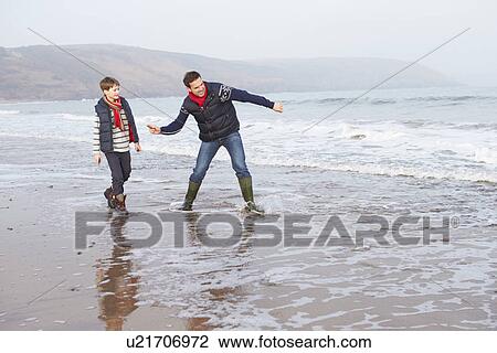 Stock Image - Father And Son Walking On Winter Beach And Throwing Stones. Fotosearch