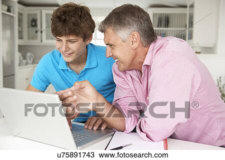 Stock Image - Father and teenage son using laptop. Fotosearch
