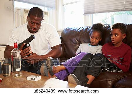 Father Checks Gun As Children Sit Next To Him On Sofa View Large Photo Image Stock Photo - Father Checks Gun As Children Sit Next To Him On Sofa. Fotosearch