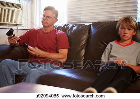 Stock Photography - Father Checks Gun As Son Sits Next To Him On Sofa. Fotosearch