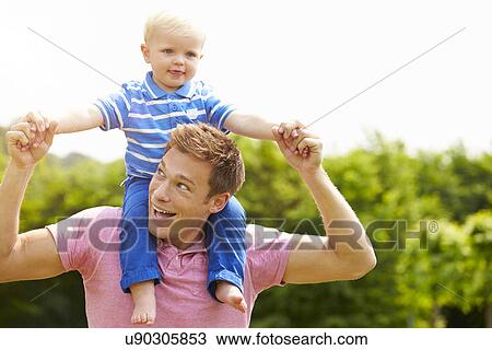 Stock Image - Father Giving Young Son Ride On His Shoulders In Garden. Fotosearch