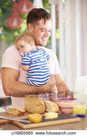 Father Holding Baby And Making Snack Whilst Using Laptop View Large Photo Image Stock Photography - Father Holding Baby And Making Snack Whilst Using Laptop. Fotosearch