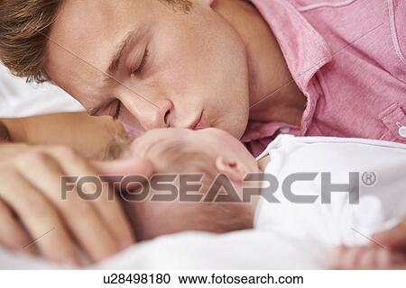 Stock Image - Father Kissing Baby Girl As They Lie In Bed Together. Fotosearch