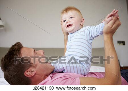 Father Playing With Baby Son As They Lie In Bed Together View Large Photo Image Stock Image - Father Playing With Baby Son As They Lie In Bed Together. Fotosearch
