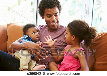 Stock Image - Father Relaxing On Sofa With Young Children. Fotosearch