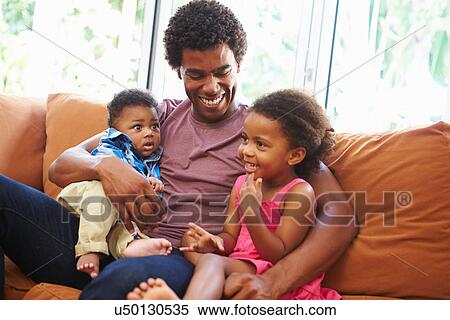 Stock Photography - Father Relaxing On Sofa With Young Children. Fotosearch