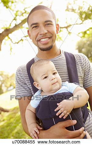 Stock Photography - Father With Son In Baby Carrier Walking Through Park. Fotosearch