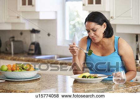 Stock Photo - Fed Up Overweight Woman Eating Healthy Meal in Kitchen. Fotosearch