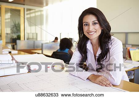 Stock Image - Female Architect Studying Plans In Office. Fotosearch