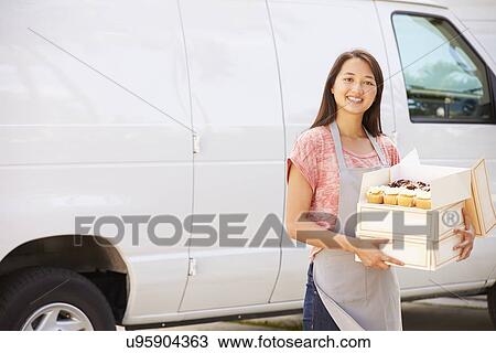 Stock Image - Female Baker Delivering Cakes Standing In Front Of Van. Fotosearch