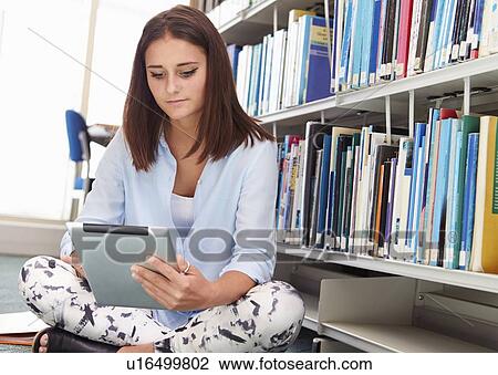 Stock Image - Female College Student Studies In Library On Digital Tablet. Fotosearch