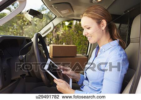 Stock Image - Female Delivery Driver Sitting In Van Using Digital Tablet. Fotosearch