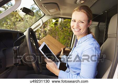 Stock Image - Female Delivery Driver Sitting In Van Using Digital Tablet. Fotosearch